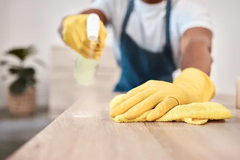 Manos de hombre negro y botella de spray y paño de limpieza en la mesa de la casa, escritorio en casa o mostrador de edificio de oficinas, guantes de zoom y producto de bacterias de tela para el mantenimiento de la higiene y el bienestar de la atención médica